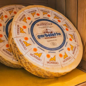 Forme di formaggio Montasio DOP adagiate su uno scaffale