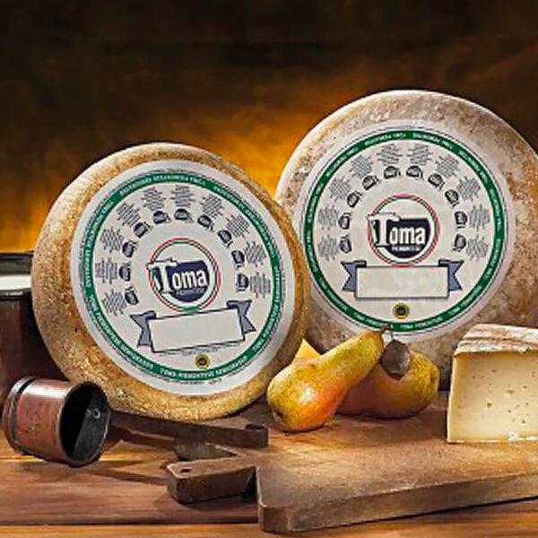 Due forme di formaggio Toma Piemontese DOP su un tagliere con delle pere